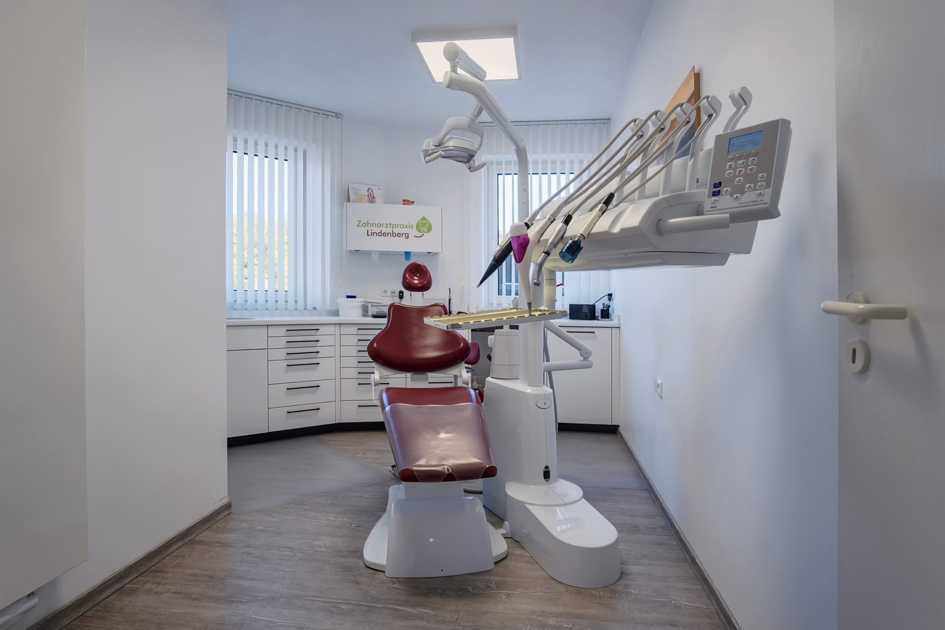 Helles Behandlungszimmer mit rotem Behandlungsstuhl